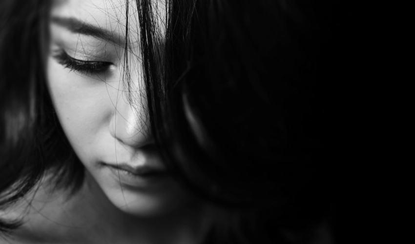 Black and white closeup of a dark-haired woman looking down anxiously due to dental fear