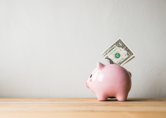 A one dollar bill sits atop a pink piggy bank used for saving money after receiving quality, affordable dental care