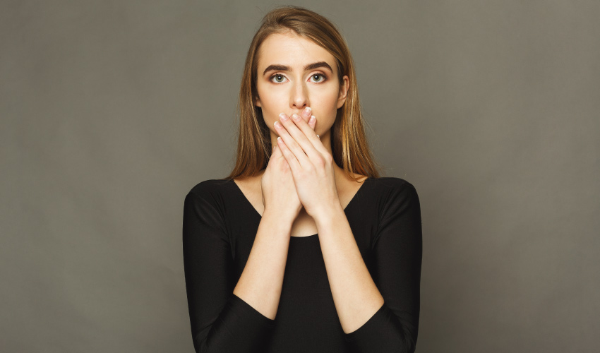 Blonde woman wearing a black shirt covers her mouth due to a white film on her tongue