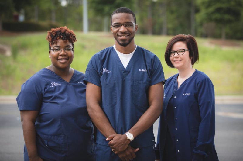 Dr. Bethea and 2 members of the Bethea Family Dentistry team wearing blue scrubs outside smiling