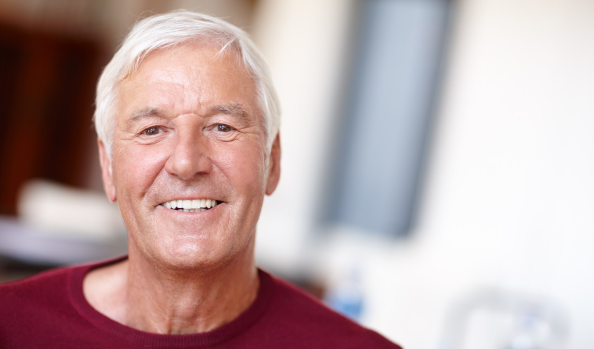 White-haired man wearing a red shirt smiles with his dentures