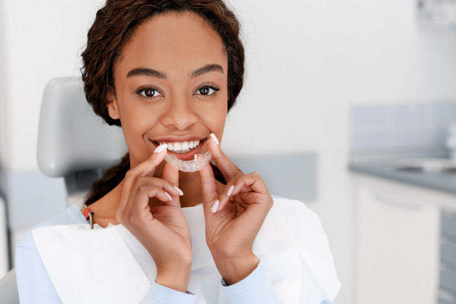 Pretty smiling black girl holding an Invisalign clear aligner in the dentist office