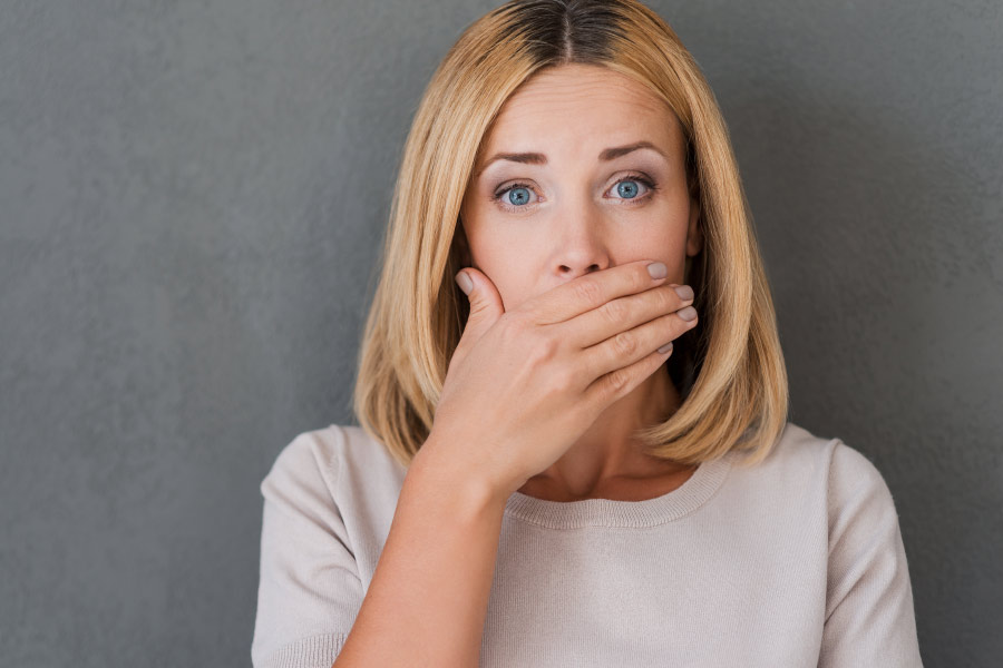 Blonde woman covering her mouth with her hand because of concern about bad breath.