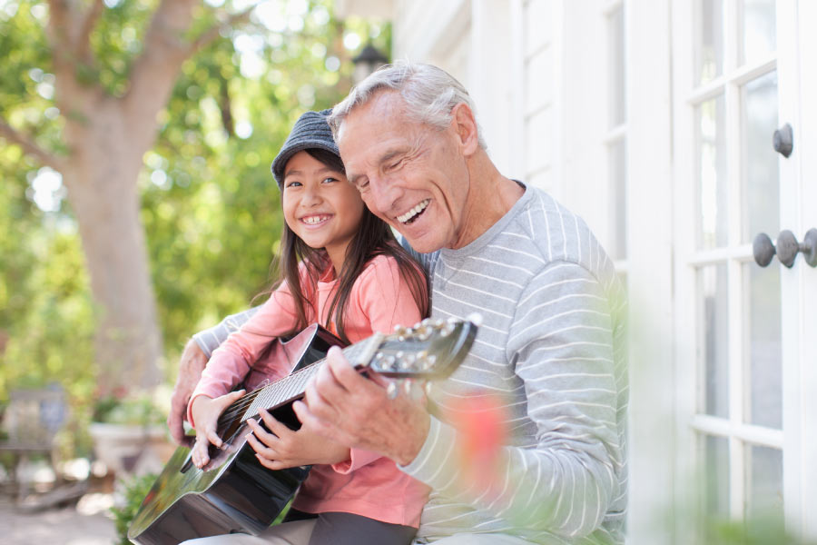 Smiling grandpa playing guitar with granddaughter.