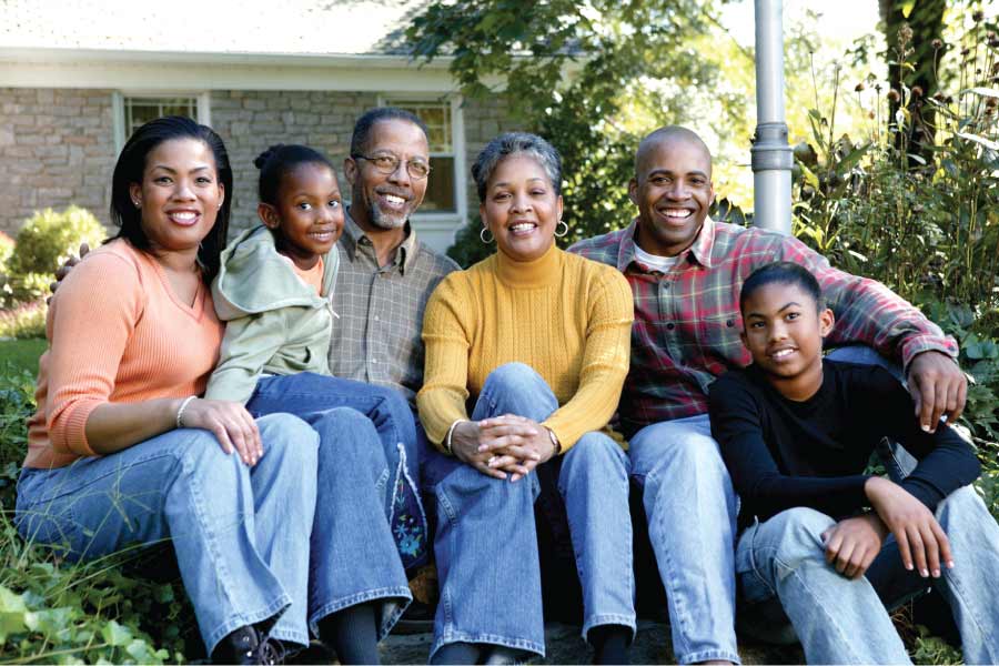 Multi-generational black family sitting together in front of a house.