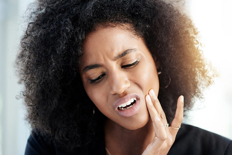 Woman touching her cheek and grimacing due to tooth pain.